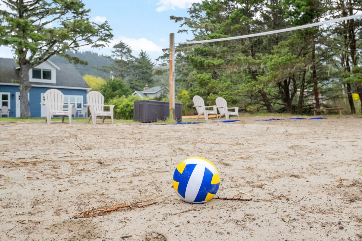 An exterior shot featuring a volleyball net set up on a sandy area, beach chairs for relaxation, and surrounding trees. The lively setup hints at group activities, playfulness, and outdoor bonding moments.
