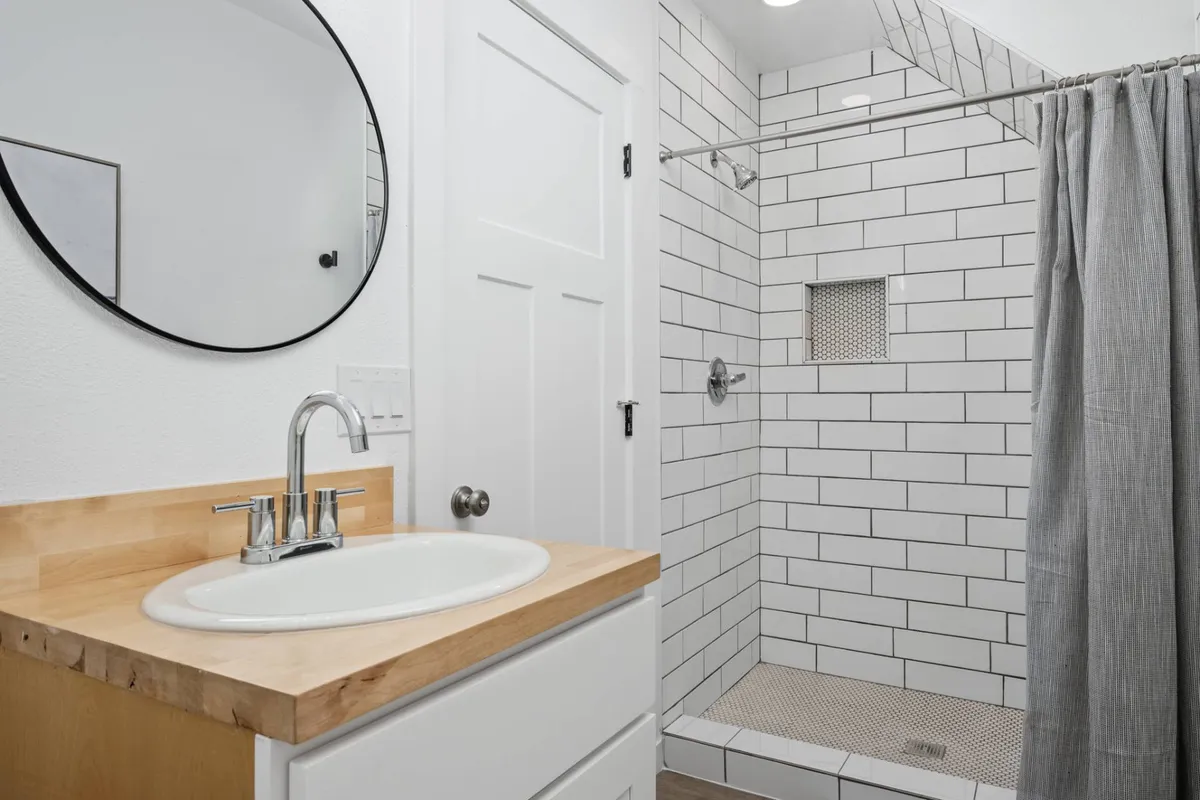 A modern, sparkling clean bathroom with a sleek sink and modern faucet, a large mirror, and a glass-enclosed shower area. The space feels inviting and stocked for convenience.