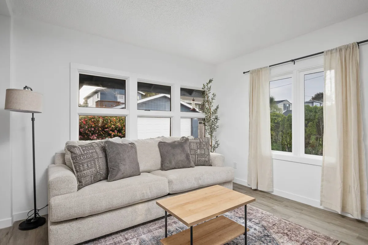 A cozy living room with a comfortable sofa, a coffee table, and large windows letting in abundant natural light. The setup encourages relaxation, reading, and conversation in a sun-drenched environment.