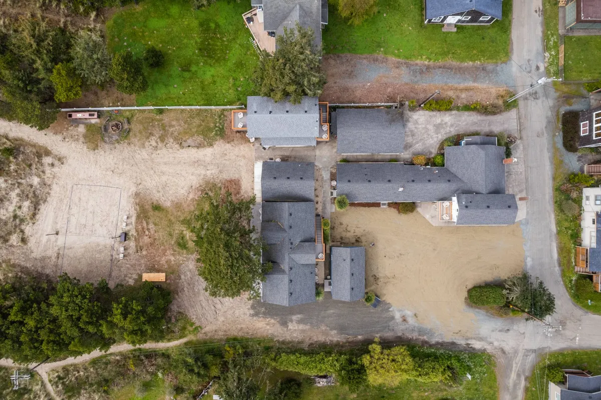 A cluster of inn buildings embraced by an open sandy area, with plenty of room for outdoor sports and gatherings. The surrounding greenery provides a peaceful, natural backdrop, and the scene suggests space for communal activities like volleyball or group games.