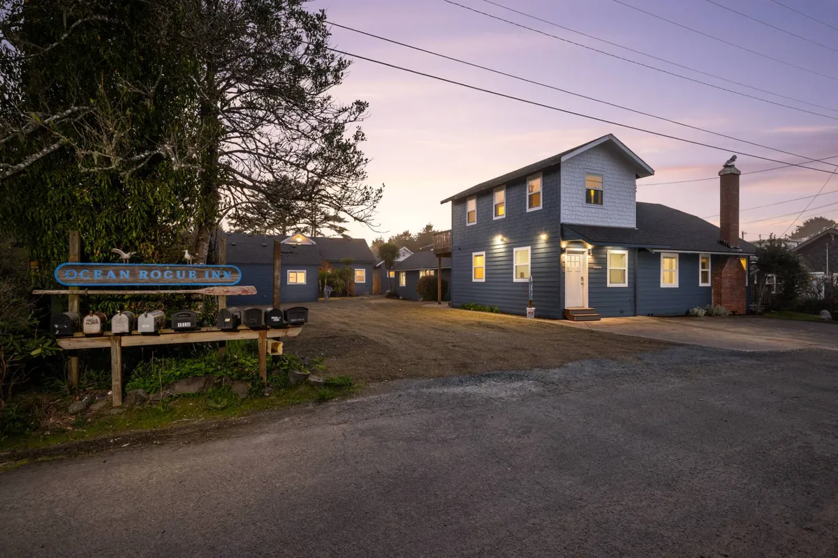 This image shows the Ocean Rogue Inn's blue exterior, featuring a welcoming sign, the inn's entrance, and a chimney, set against a tranquil sky. The warm, approachable vibe makes it clear that this is the starting point for a beachside adventure, and the exterior clearly signals the inn's identity and hospitality.