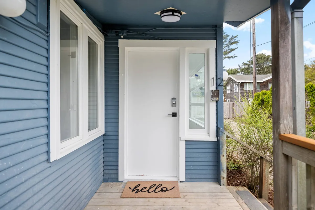 The welcoming front door of the property, complete with a cheerful welcome mat and large windows. The scene hints at the inviting atmosphere awaiting inside while displaying the property’s beachside character.
