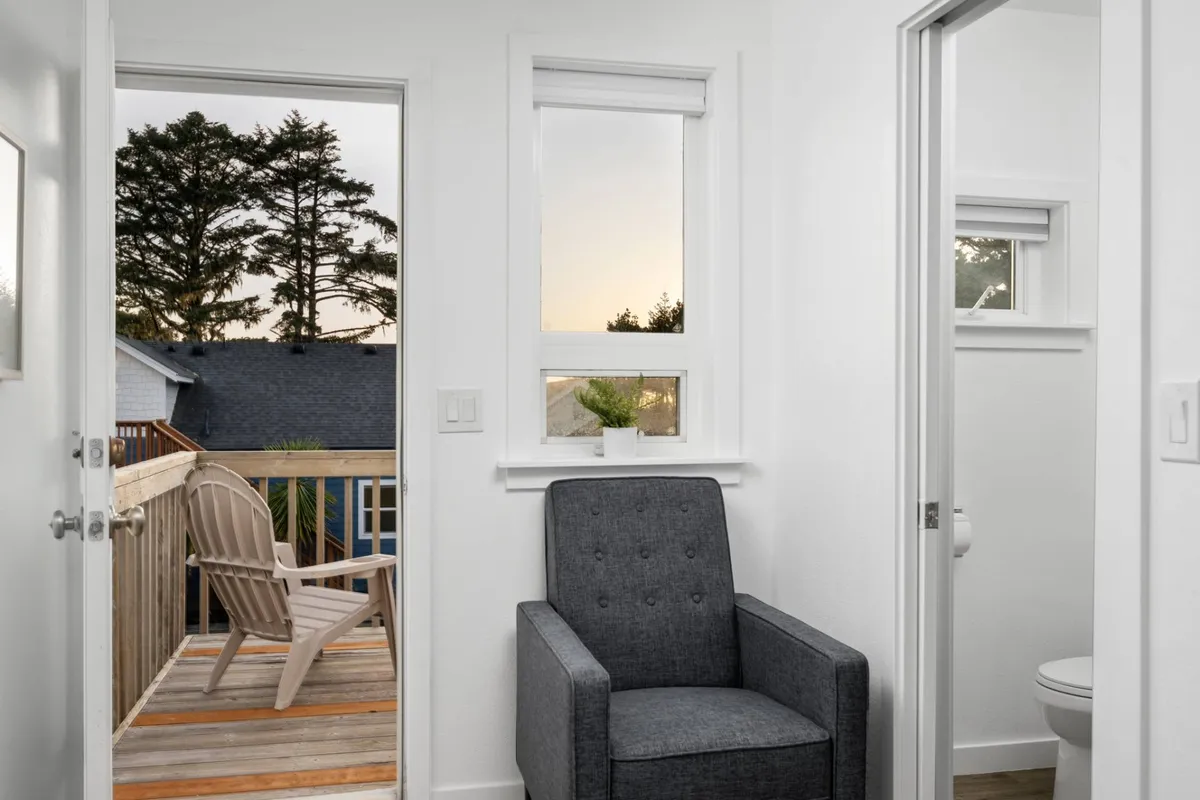 A cozy armchair placed near windows that look out onto a deck and surrounding trees. The light streaming in creates a serene setting, perfect for reading or enjoying a peaceful moment while still visually connecting to the outside world.
