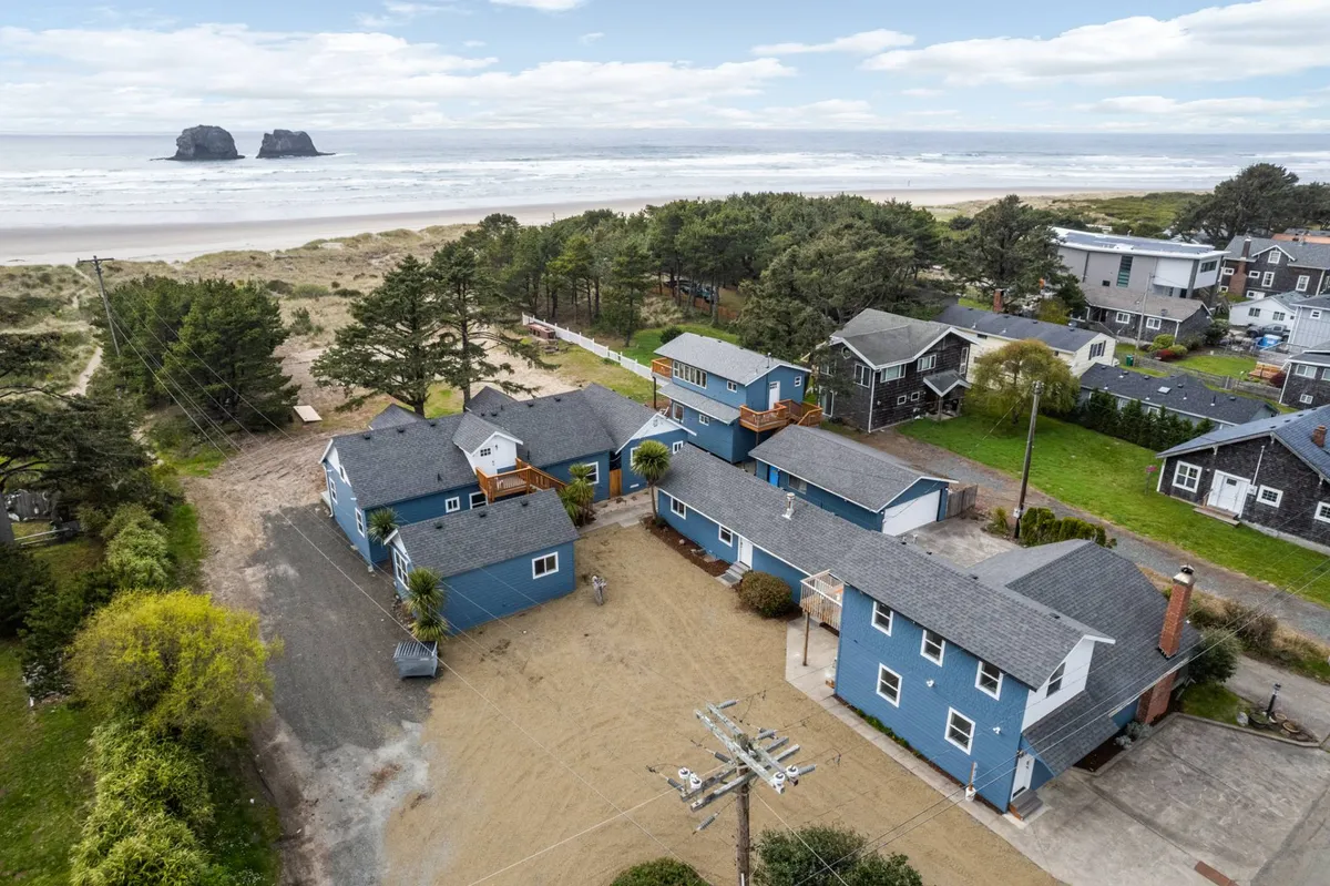 A relaxed scene showing the blue buildings of the Ocean Rogue Inn with a sandy area leading directly to the ocean. The view exudes a casual, inviting beachside atmosphere, with open space for gatherings and play.