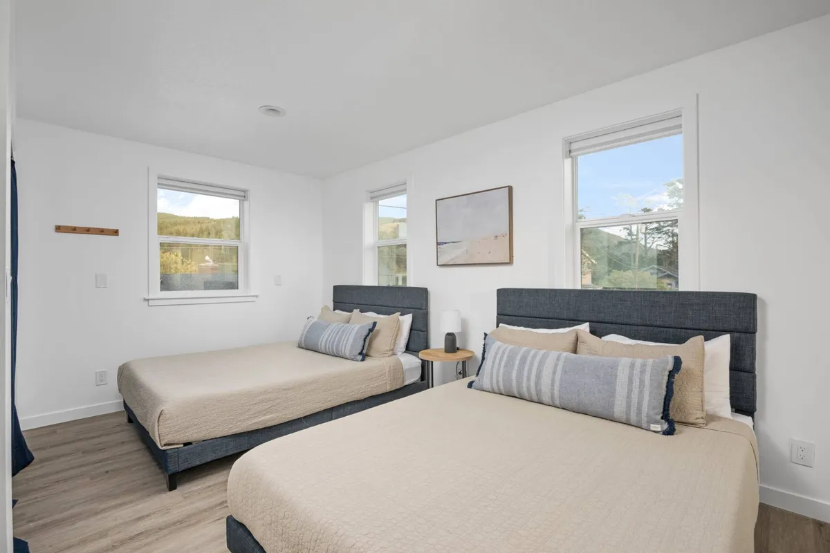 An inviting bedroom featuring two beds, cozy linens, and sunlight streaming through the window, complemented by abstract artwork on the wall. The space feels both relaxing and flexible, ideal for families or friends traveling together.