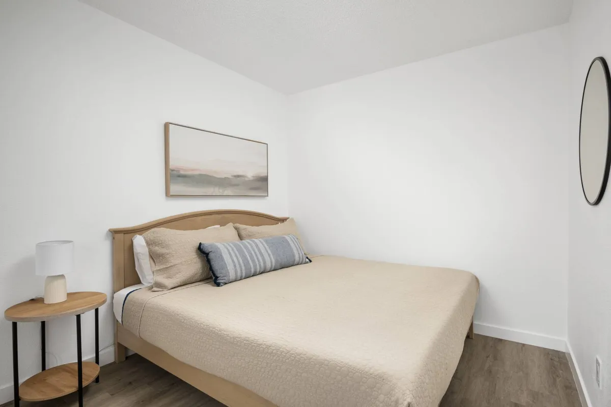 A tranquil bedroom with a comfortable bed, nightstand, lamp, and calming artwork above the headboard. Soft lighting and minimal decor create a peaceful atmosphere, perfect for restful sleep.